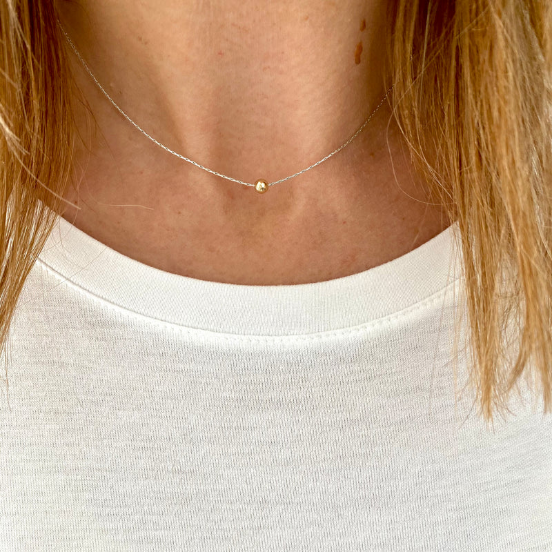 Dainty silver necklace with a simple shiny gold bead.