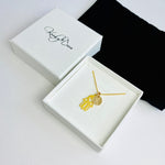 Pretty ribbon sign necklace with hamsa hand charm raising funds for cancer research. Necklace arrives in a white box.