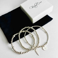 Personalised stacking bracelet set with three silver bracelets. Perfect stacking bracelet gift set for her with an alphabet charm. Silver bracelet set with personalised disc charm, angel wing charm and plain bead bracelet in sterling silver.